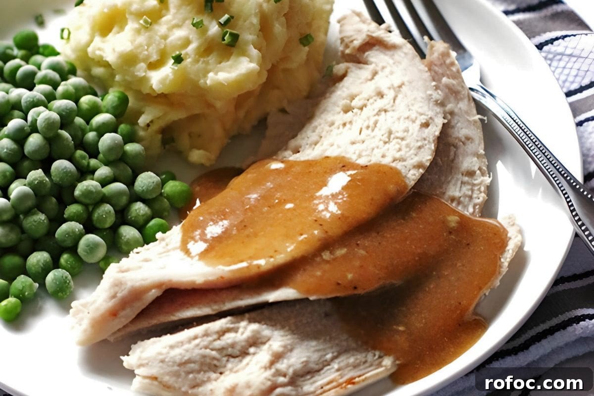 12 Delicious Easter Crockpot Recipes for a Stress-Free Holiday 12 A plate of sliced roast turkey covered in brown gravy, accompanied by mashed potatoes with chives and a serving of green peas.