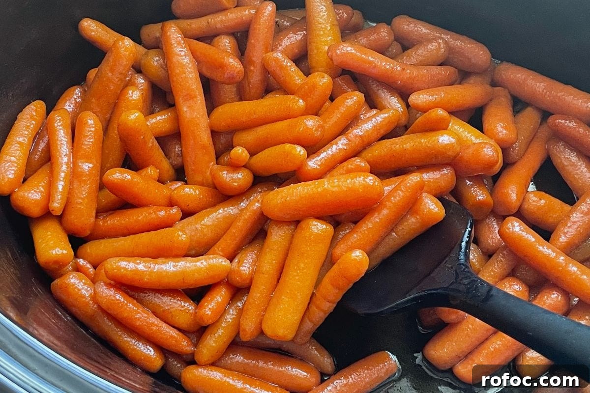 12 Delicious Easter Crockpot Recipes for a Stress-Free Holiday 10 A close-up view of shiny glazed baby carrots in a black cooking pot with a black spatula.