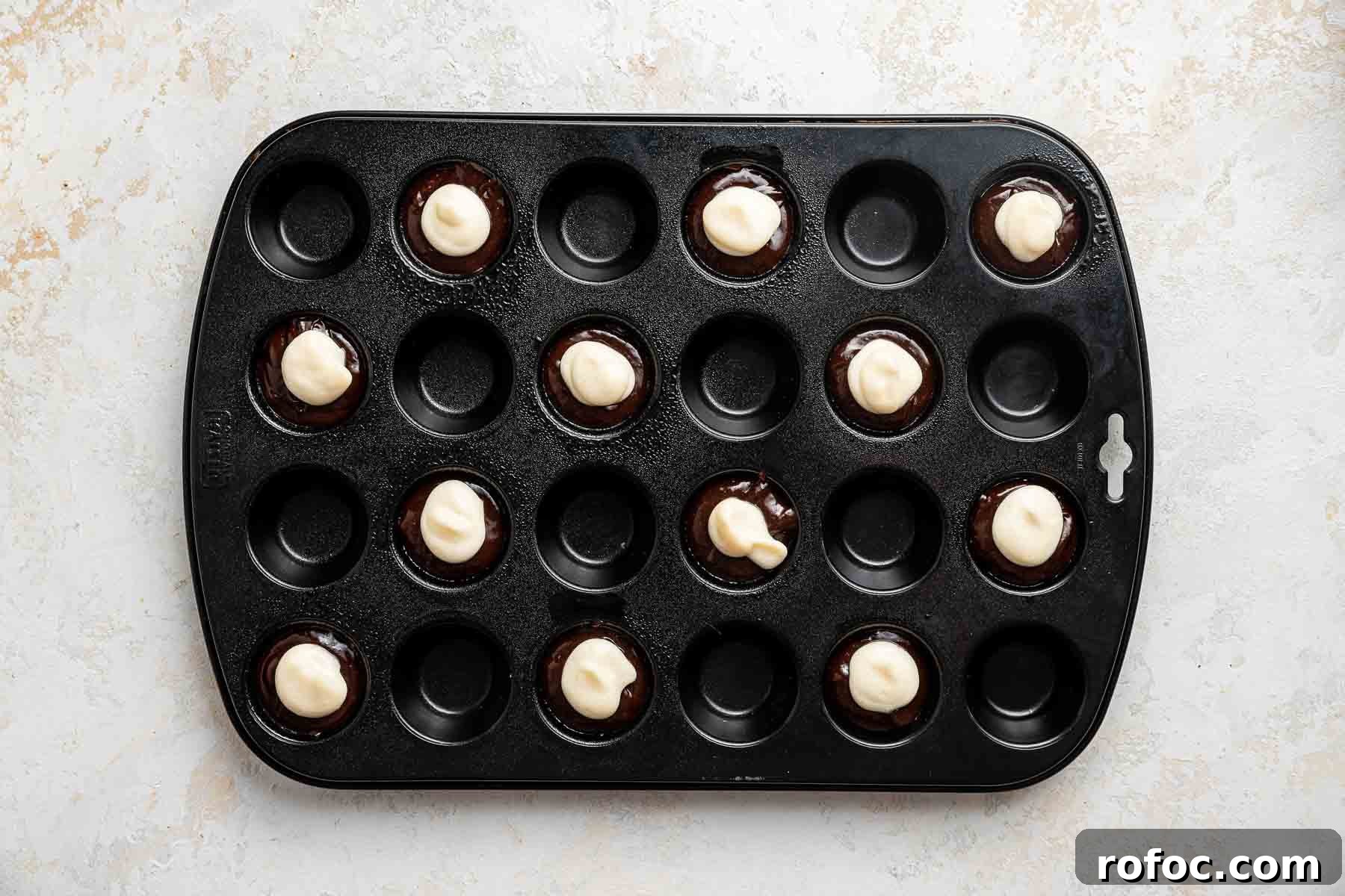 Cheesecake Brownie Bites: Mini Dessert Recipe for Parties 12 Dolloping cheesecake batter on cheesecake brownie bites.