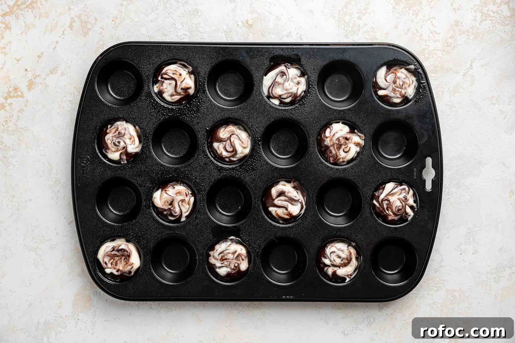 Cheesecake Brownie Bites: Mini Dessert Recipe for Parties 13 Swirled cheesecake brownie bites, before baking in a black mini muffin pan.