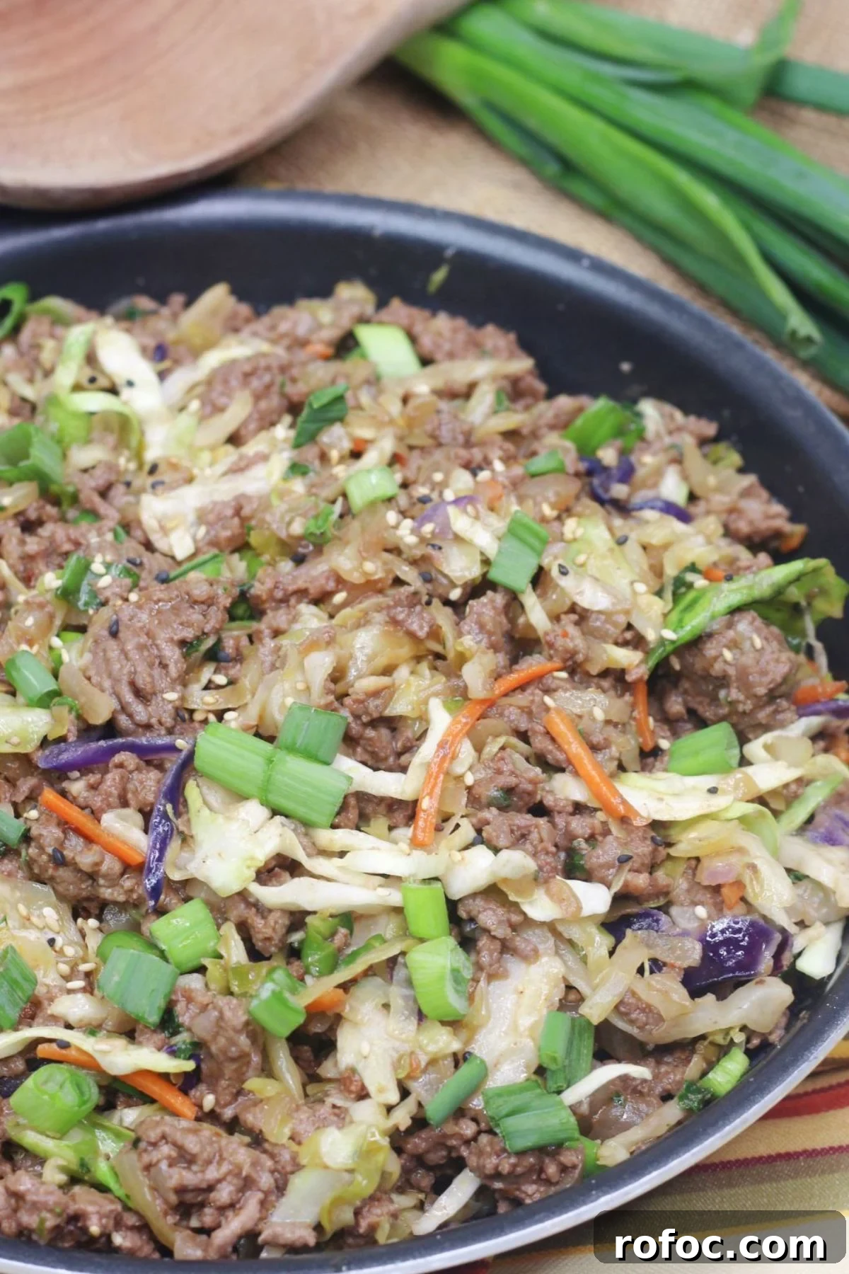 Gluten-Free Inside-Out Egg Roll Recipe for Crispy Flavor 2 Inside out egg roll in a skillet with green onions on top and a wooden spoon and white plates behind it.