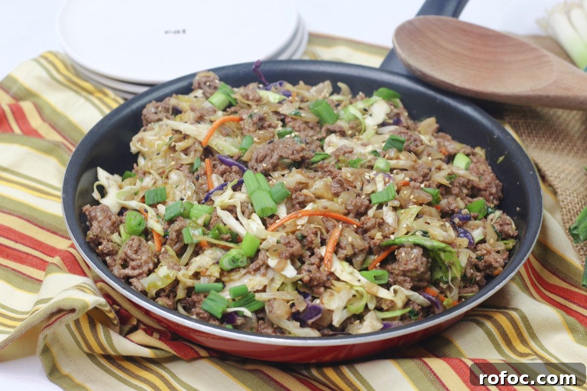 Gluten-Free Inside-Out Egg Roll Recipe for Crispy Flavor 12 Inside out egg roll in a skillet with green onions on top and a wooden spoon and white plates behind it.