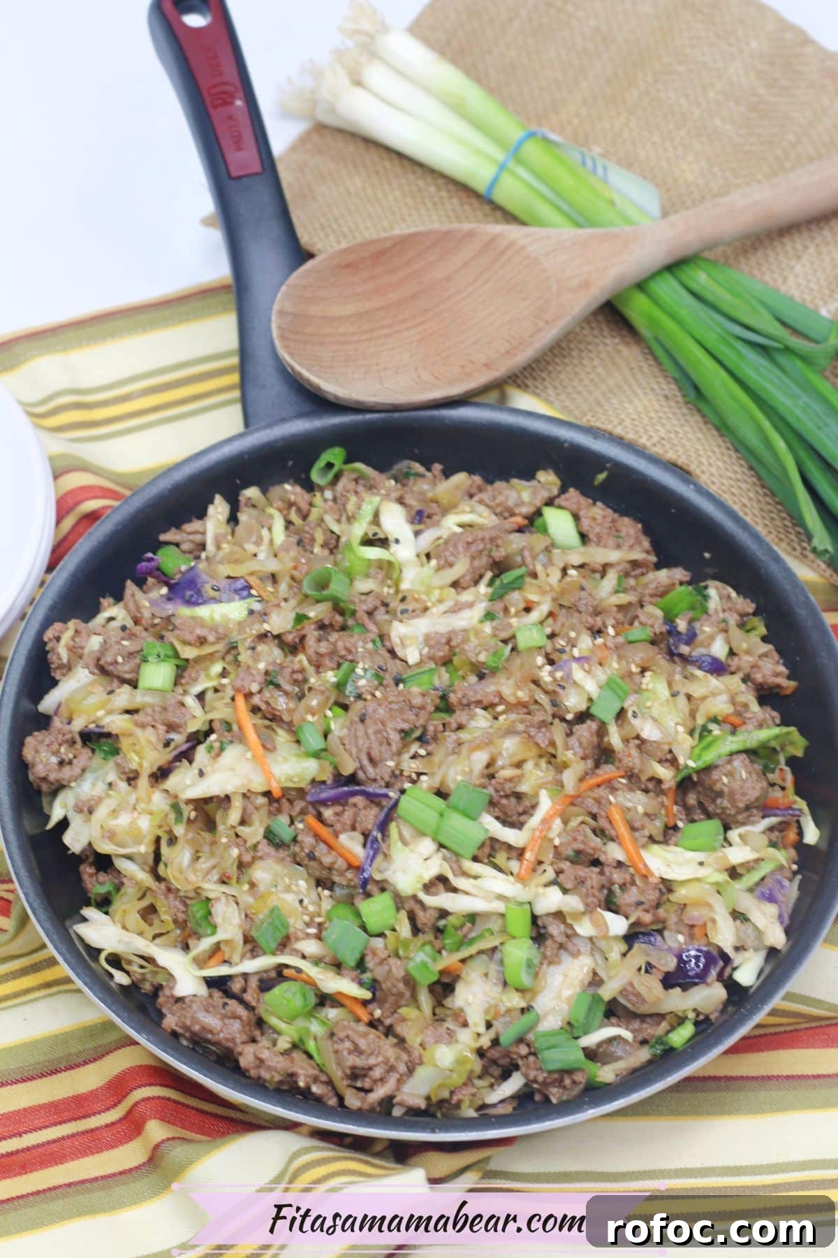 Gluten-Free Inside-Out Egg Roll Recipe for Crispy Flavor 7 Inside out egg roll in a skillet with green onions on top and a wooden spoon and white plates behind it.