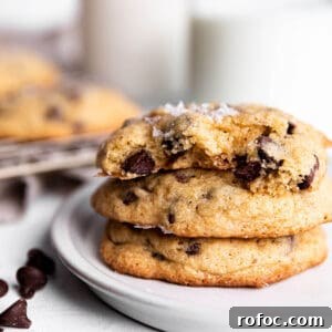 A stack of 3 sourdough chocolate chip cookies with milk in the back.