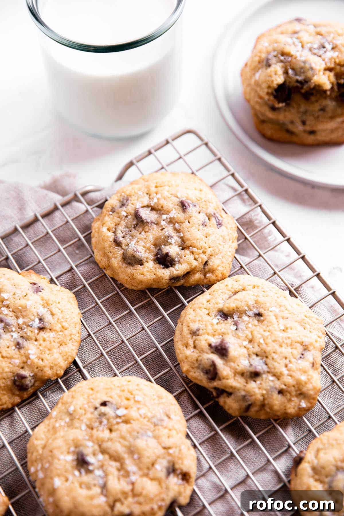 A cooling rack with chocolate chip cookies with a glass of milk.