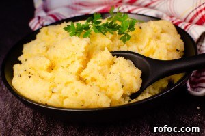 Buttered Swede in a black bowl with a black serving spoon and a red and white towel in the background