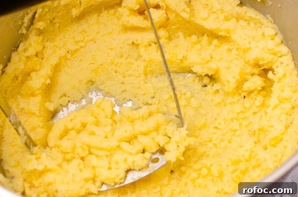 Mashing up the Creamy Buttered Swede in a silver pot with a silver masher