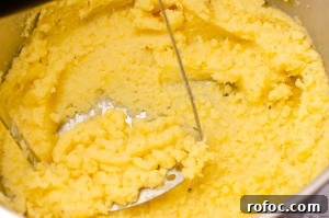 Mashing up the Creamy Buttered Swede in a silver pot with a silver masher