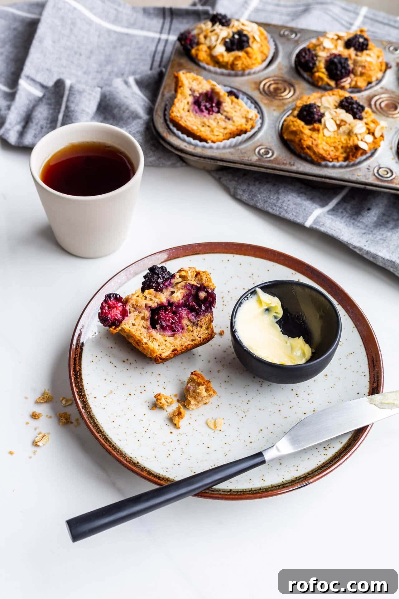 Hearty Apple and Blackberry Muffins Recipe for Fall Baking 7 Hearty apple blackberry muffins with oats, one split open on a plate with butter and a knife, served with black tea