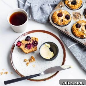 A plate with an apple blackberry muffin split open, served with butter and a cup of tea.
