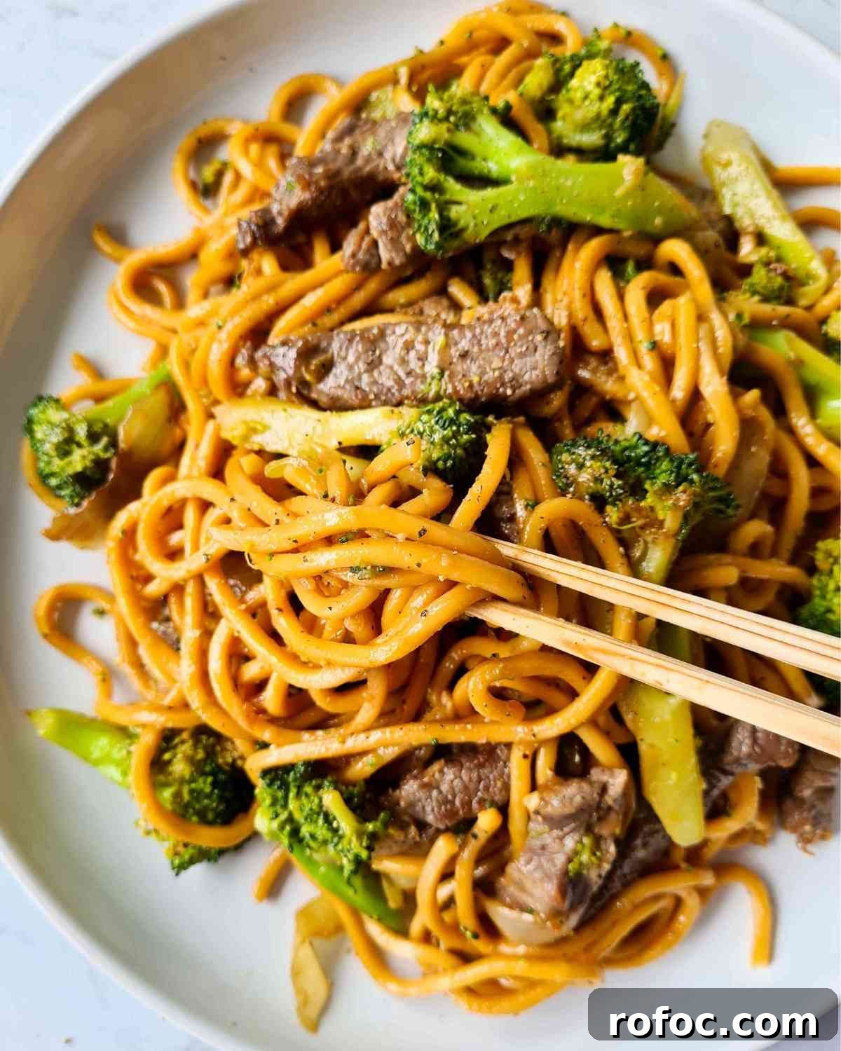 Beef and Broccoli Stir-Fry Noodles Recipe 12 Stir fried noodles with broccoli, beef strips on a large white plate and a pair of chopsticks