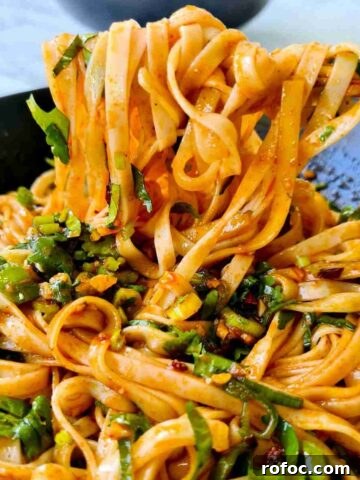 Spicy noodles being held up by a pair of chopsticks from a black bowl
