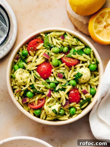 Vegetarian Orzo Pesto Salad with tomatoes, peas, and cheese in a bowl.