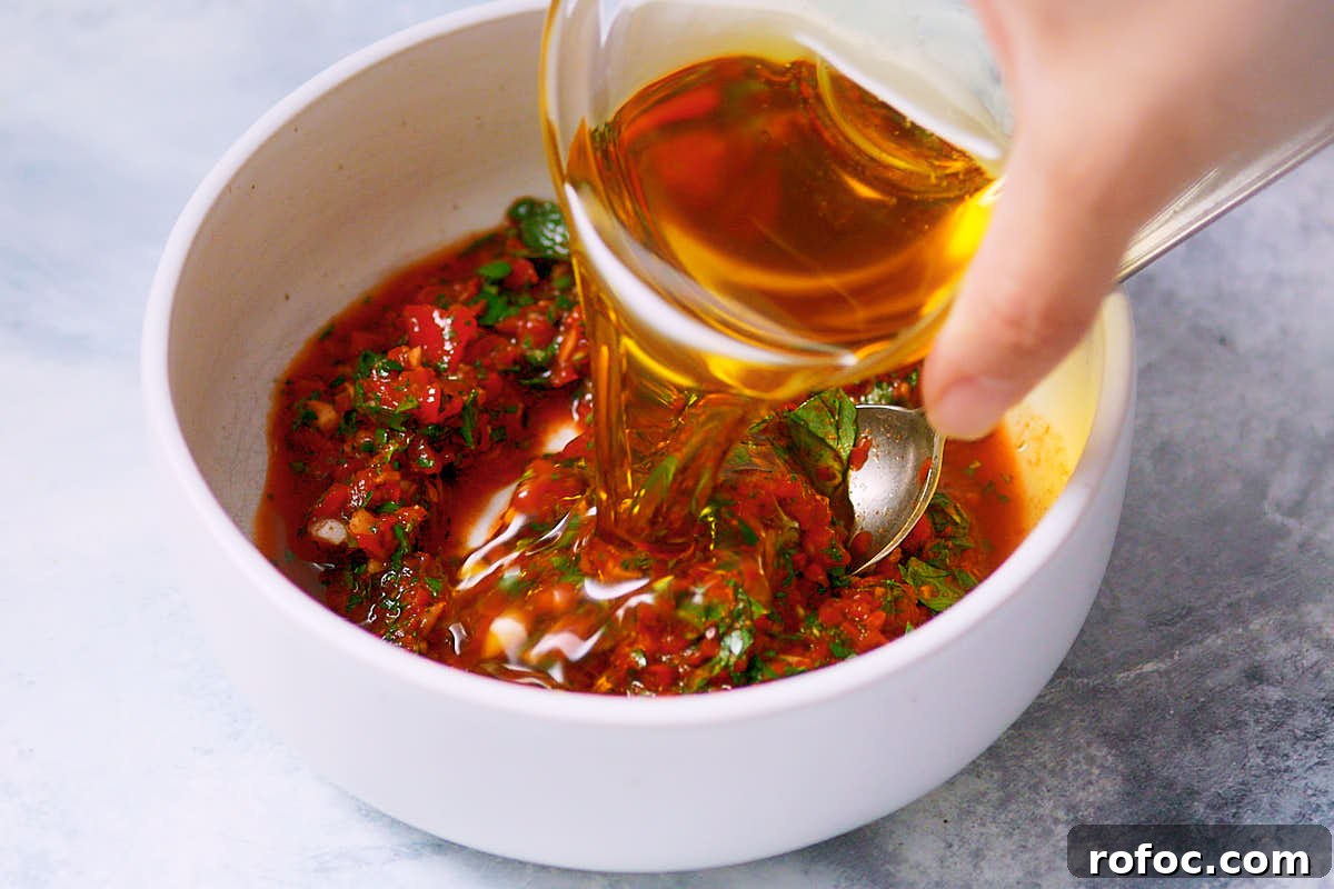 Red Chimichurri Pasta Recipe — Serve Hot or Chilled 8 Olive oil being added to a bowl of red chimichurri sauce.