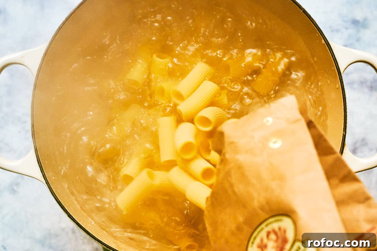 Red Chimichurri Pasta Recipe — Serve Hot or Chilled 9 Dried rigatoni pasta being poured into boiling water.