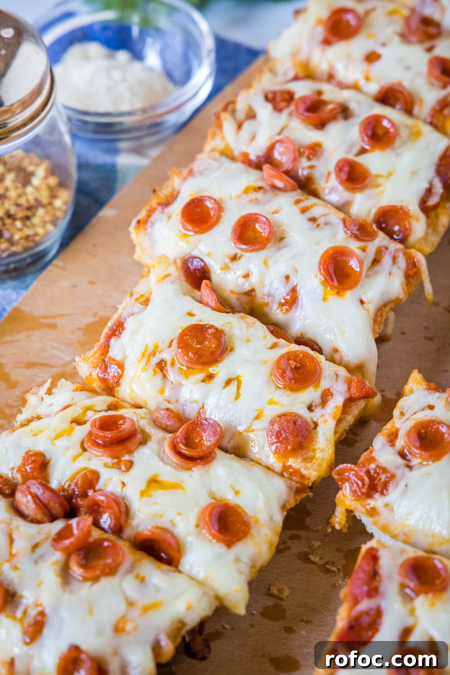French bread pizza topped with garlic butter, pizza sauce, and mozzarella French bread pizza cut into slices on a wooden cutting board.