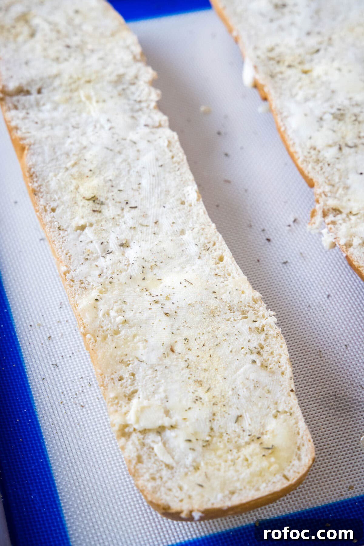 Spread with butter and add seasonings. French bread halves spread with garlic butter on a baking sheet.