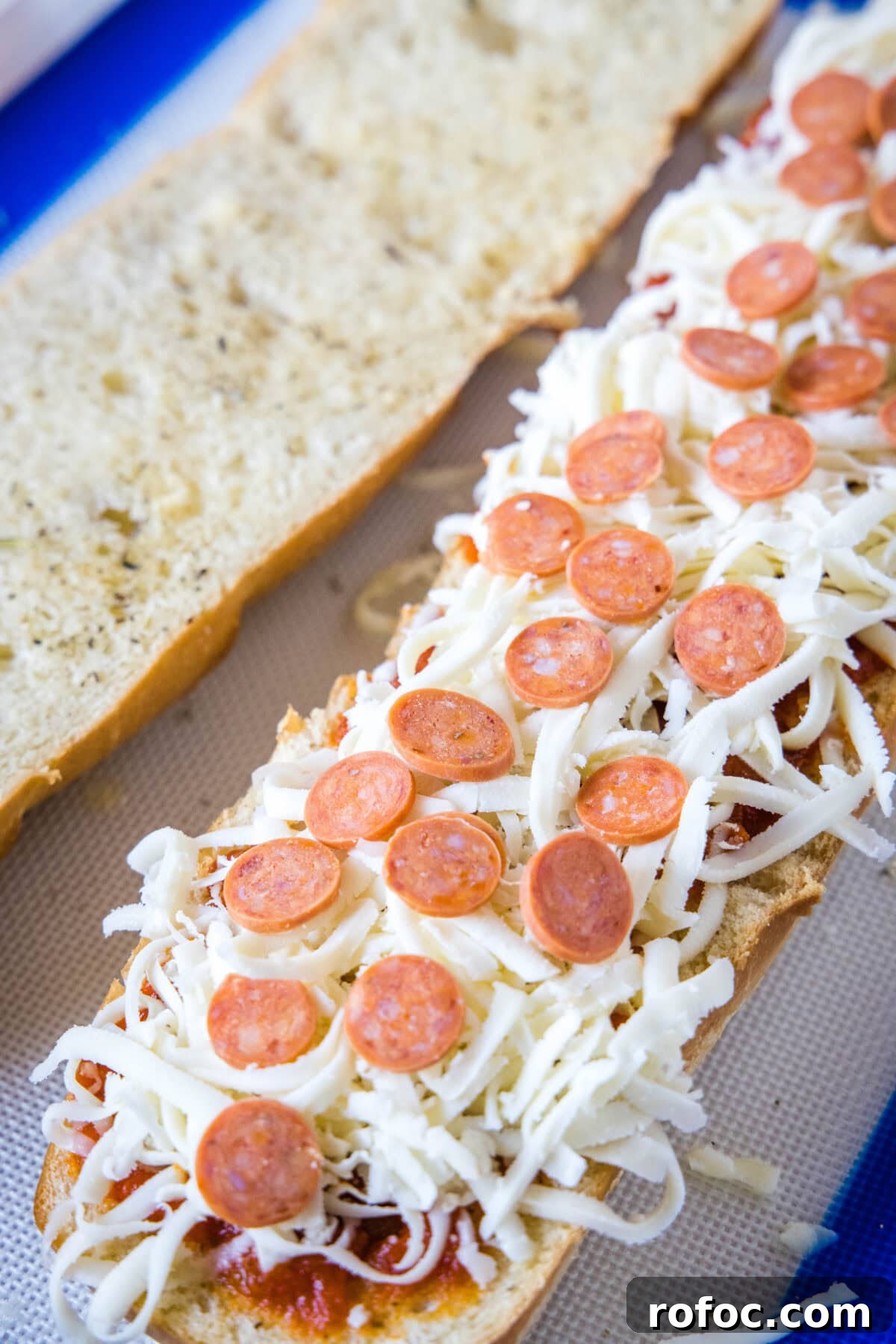 Add toppings and bake! Partially assembled French bread pizzas on a baking sheet.