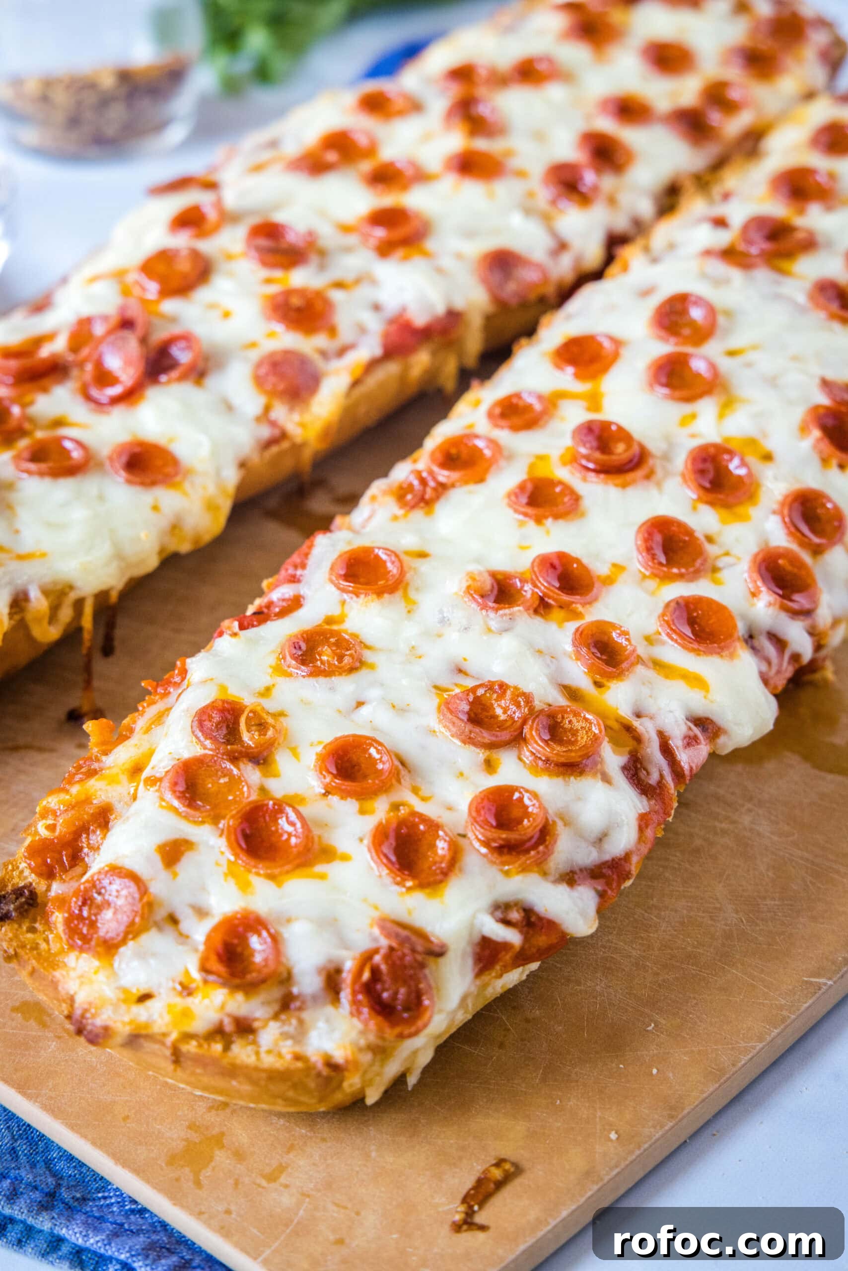 Two French bread pizzas side by side Two French bread pizzas side by side on a wooden cutting board.