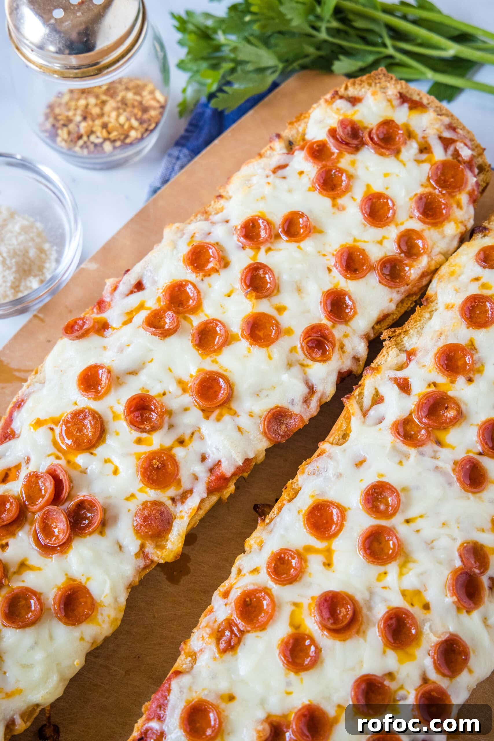 Finished French bread pizzas Two French bread pizzas side by side on a wooden cutting board.