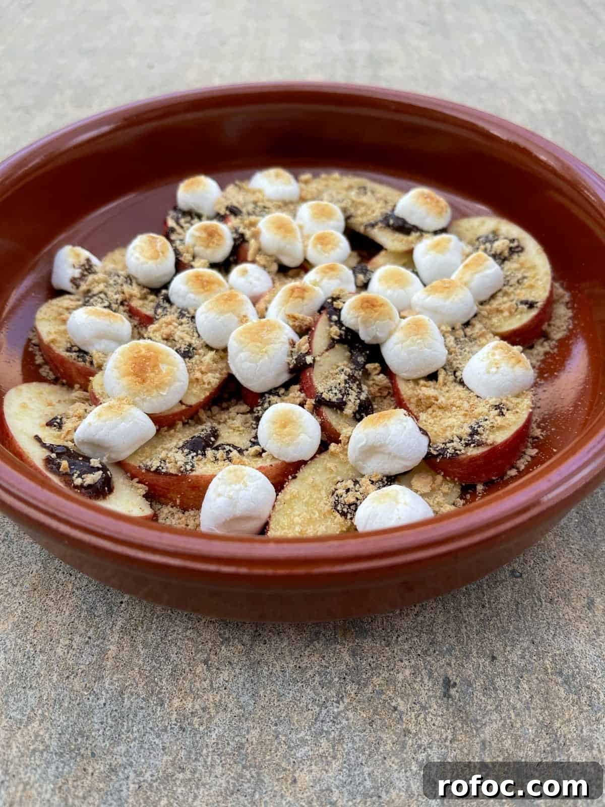 Apple S'mores Nachos: Crispy Cinnamon Apple Slices with Chocolate & Marshmallow Dip 7 Apple S'mores Dessert Nachos in orange dish on concrete.