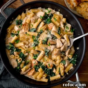 One-Pot Chicken Rigatoni Alfredo Recipe for Creamy Weeknight Meals 7 A frying pan with creamy rigatoni alfredo with chicken and kale, and grated cheese, with a spoon resting in the dish.