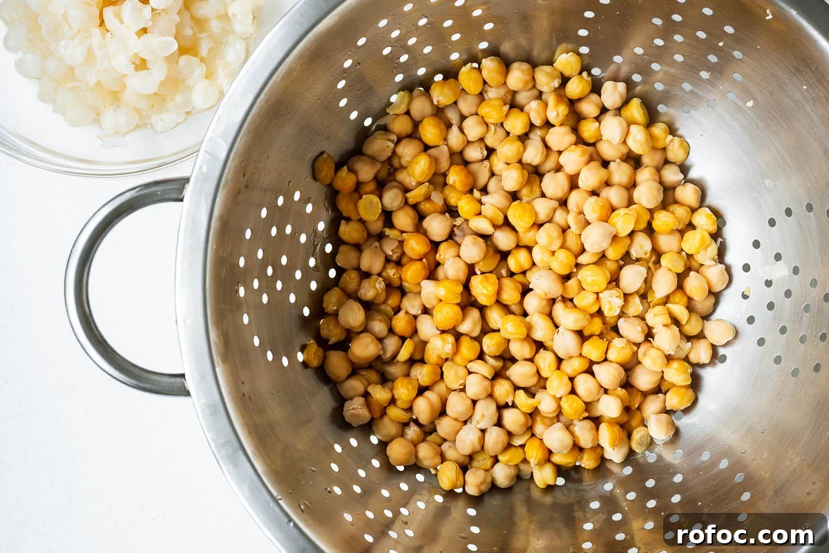 Spicy Harissa Hummus Recipe: Creamy Homemade Dip in Minutes 7 Cooked chickpeas draining in a colander next to a small bowl of chickpea skins.