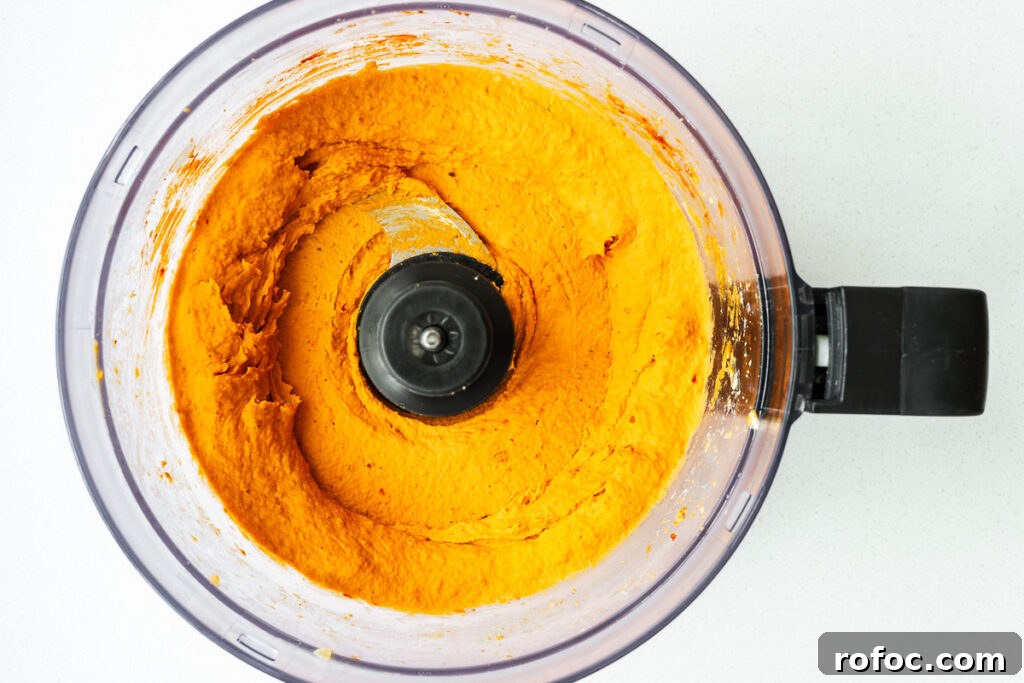 Spicy Harissa Hummus Recipe: Creamy Homemade Dip in Minutes 9 Creamy harissa hummus with a bright orange colour in a food processor bowl.