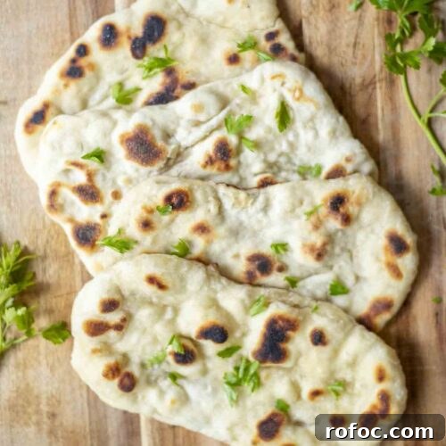 four sourdough flatbreads arranged on a wood cutting board with fresh herbs. The cutting board rests on a blue and white towel