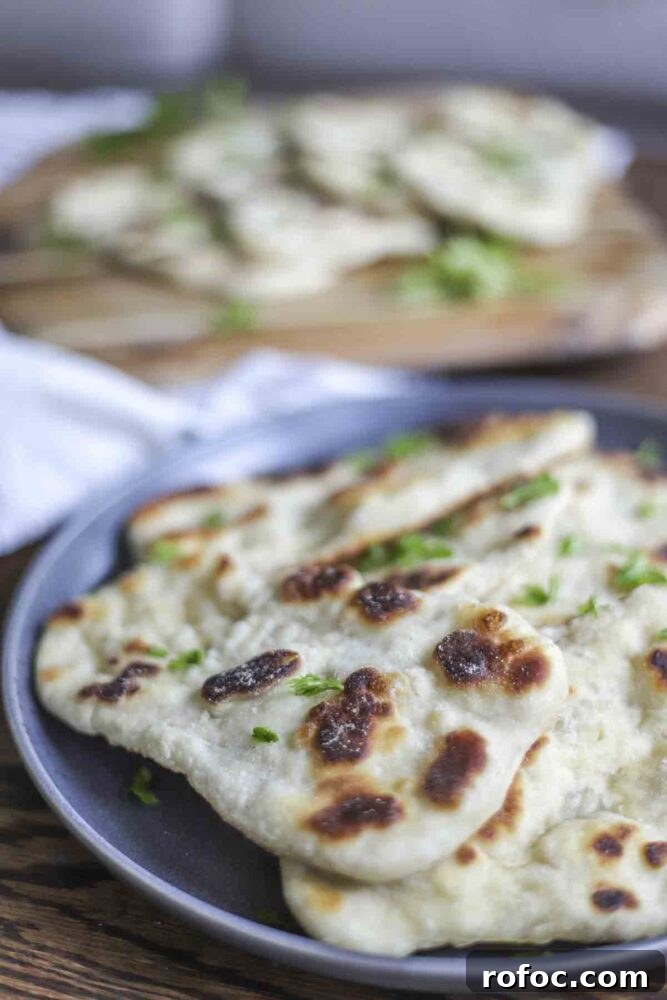 Sourdough Flatbread Recipe Using Active Starter or Discard (No Yeast) 3 sourdough flatbread piled on a dark gray plate with a cutting board of more flatbreads in the background