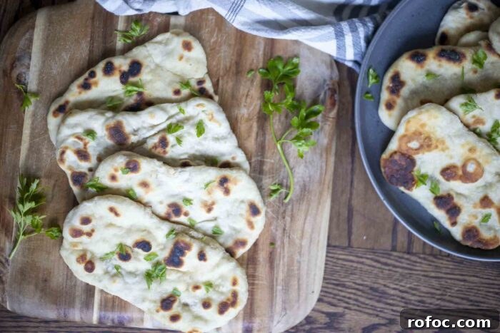 Sourdough Flatbread Recipe Using Active Starter or Discard (No Yeast) 4 four sourdough flatbreads arranged on a wood cutting board and topped with chopped herbs. A dark gray plate in the background has more flatbreads and a stripped towel