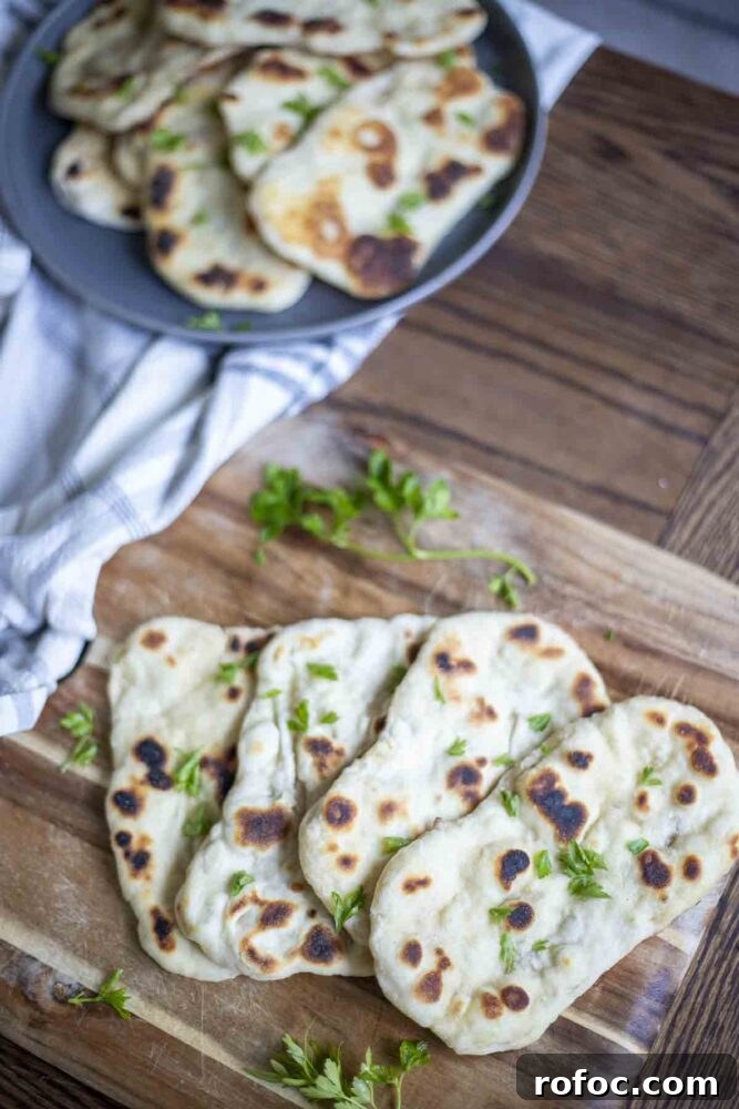 Sourdough Flatbread Recipe Using Active Starter or Discard (No Yeast) 5 four sourdough flatbreads arranged on a wood cutting board and topped with chopped herbs. A dark gray plate in the background has more flatbreads and a stripped towel