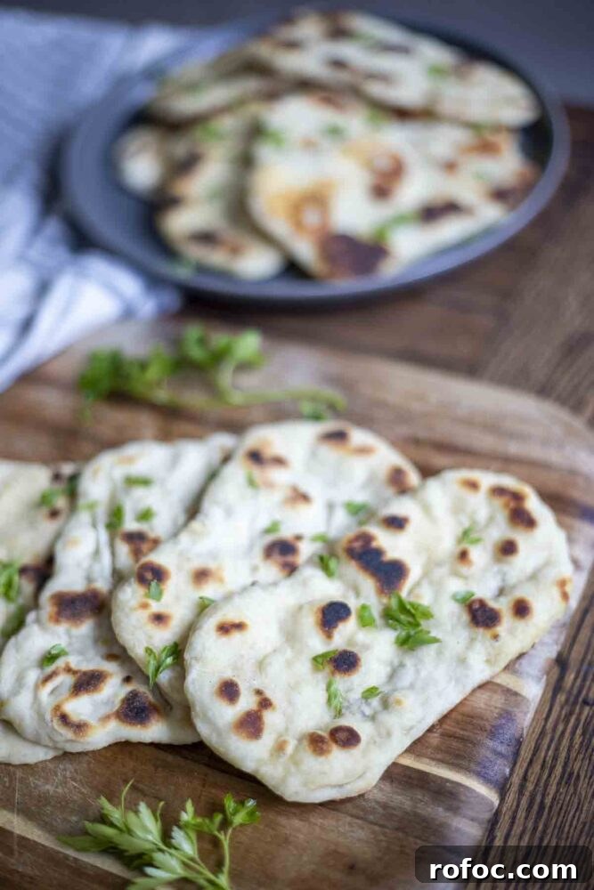 Sourdough Flatbread Recipe Using Active Starter or Discard (No Yeast) 6 four sourdough flatbreads topped with herbs on a wood cutting board. A dark gray plate on a stripped blue and white towel has more flatbreads in the background