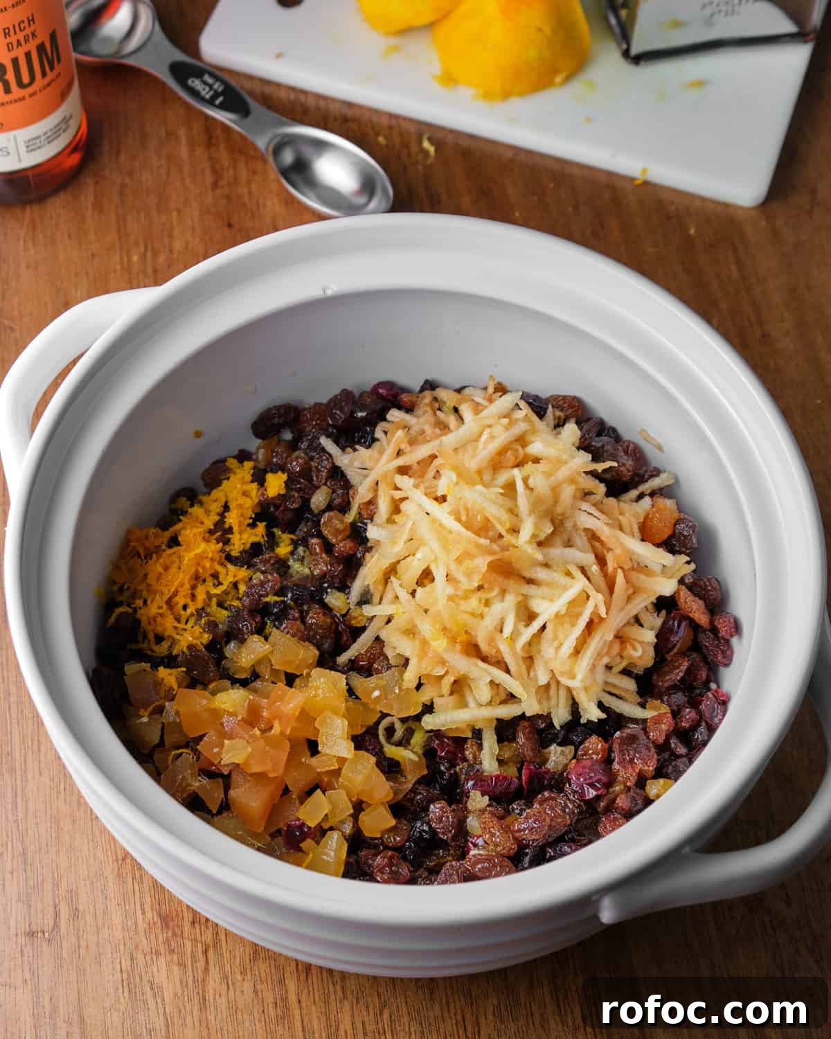 Photo of a bowl with all the dried fruits, grated ginger, orange zest and juice and rum, ready to mix together.