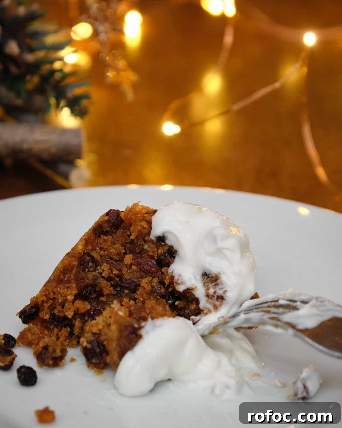 Photo of a portion of christmas pudding on a plate with vegan creme fraiche and fairy lights in the background.