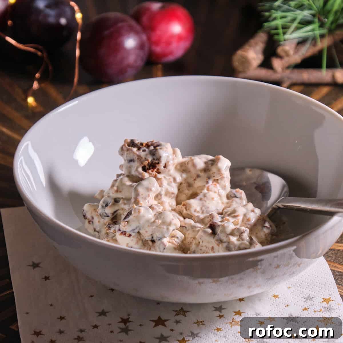 Photo of christmas pudding ice cream made from vegan vanilla ice cream and leftover christmas pudding, in a white bowl placed in a christmassy setting.