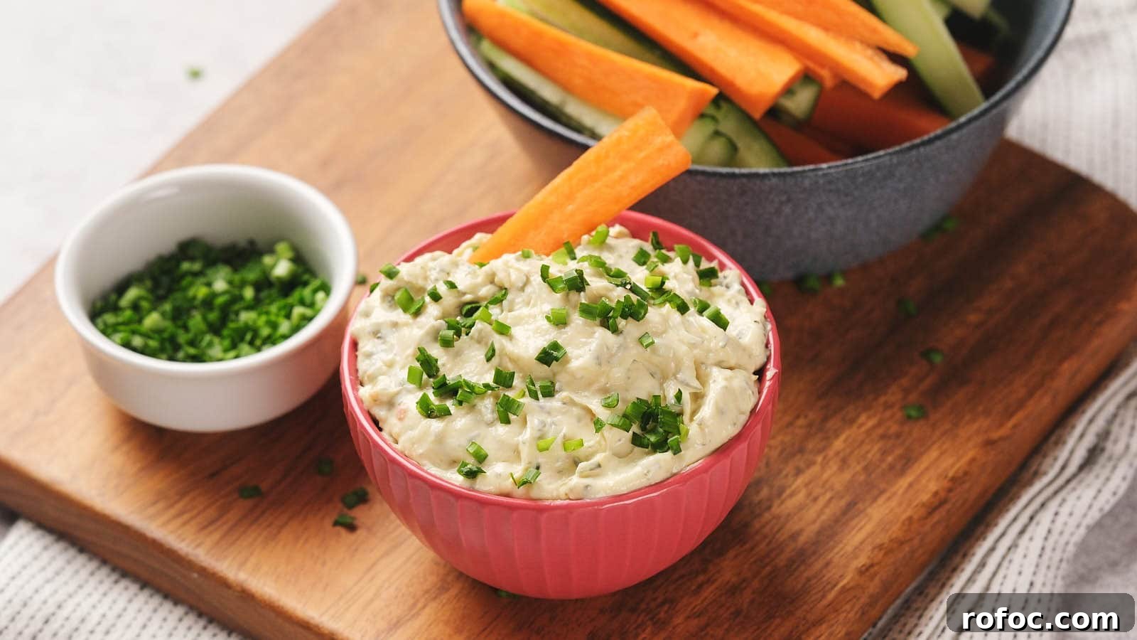 15 Low-Carb Recipes That Taste Like You Spent Hours 10 A bowl of sour cream dip garnished with chopped chives, accompanied by carrot and cucumber sticks in a bowl.