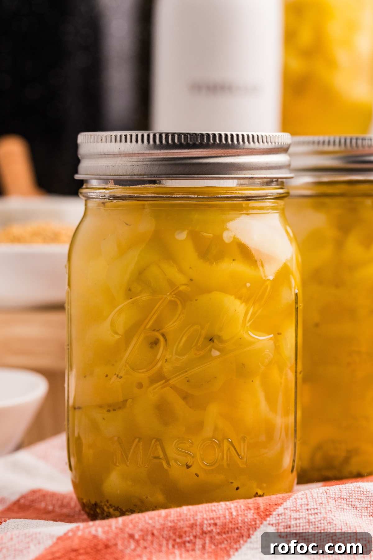 How to Can Homemade Pickled Banana Peppers for Long-Term Storage 2 sealed jar of banana peppers on red checkered cloth.