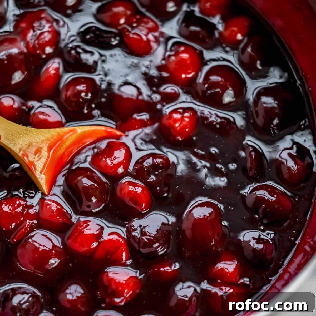 Decadent Cherry Cheesecake Recipe with a Buttery Crust 11 Finished cherry sauce in a pan, with a wooden spoon stirring.