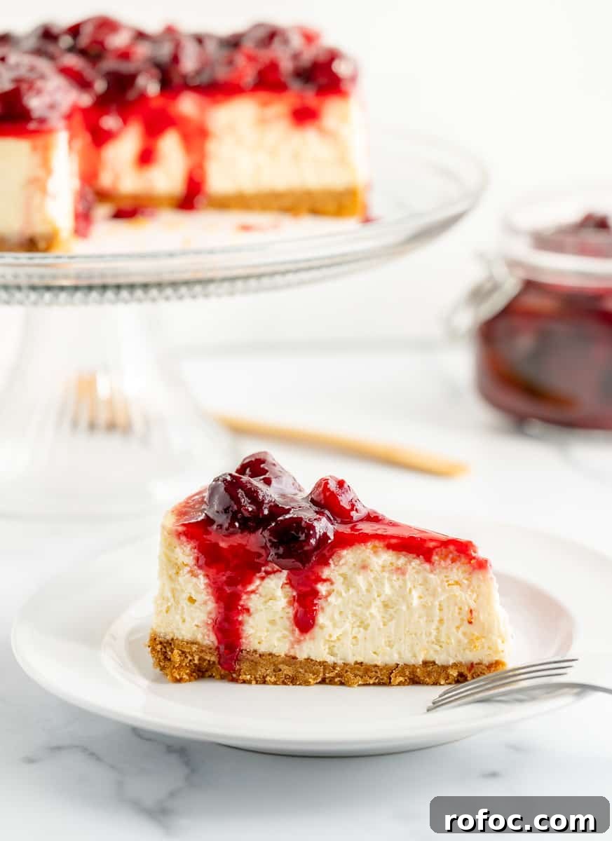 Decadent Cherry Cheesecake Recipe with a Buttery Crust 18 A slice of cheesecake on a plate with a fork. A full cheesecake and cherry sauce in the background.