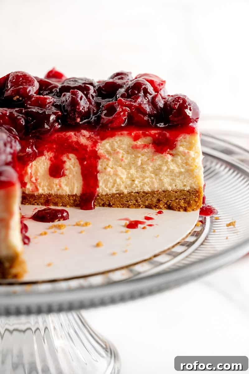 Decadent Cherry Cheesecake Recipe with a Buttery Crust 19 A cheesecake with cherry topping, a slice missing and cherry juice dripping inside.