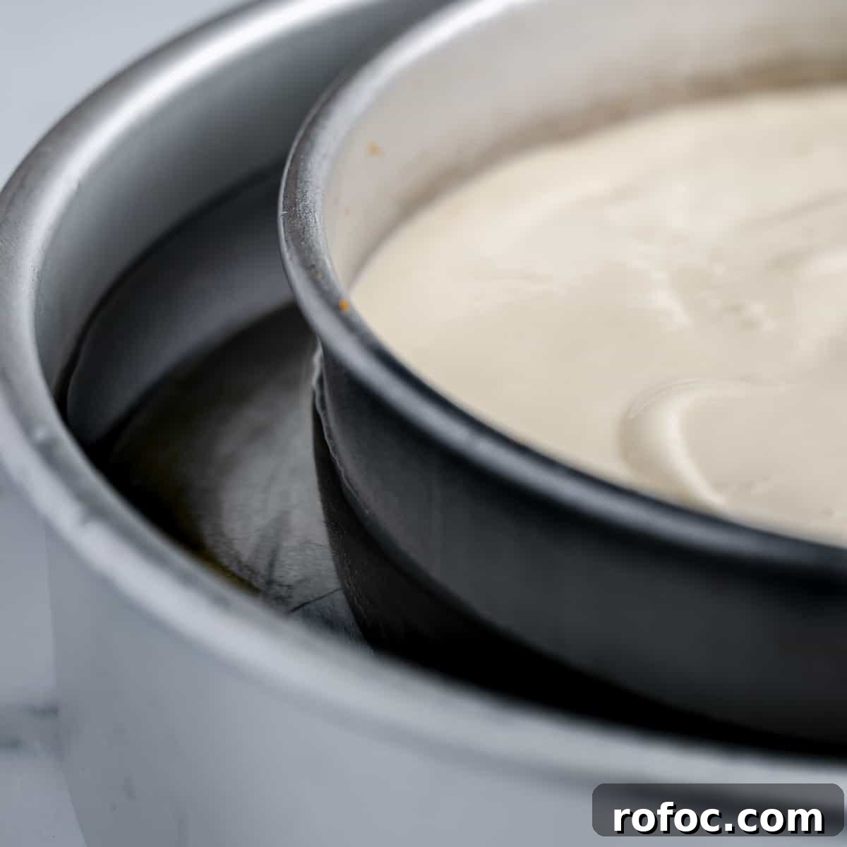 Decadent Cherry Cheesecake Recipe with a Buttery Crust 8 Showing the water level in the water bath. A small cake pan full of cheesecake batter sits in a larger pan full of water.