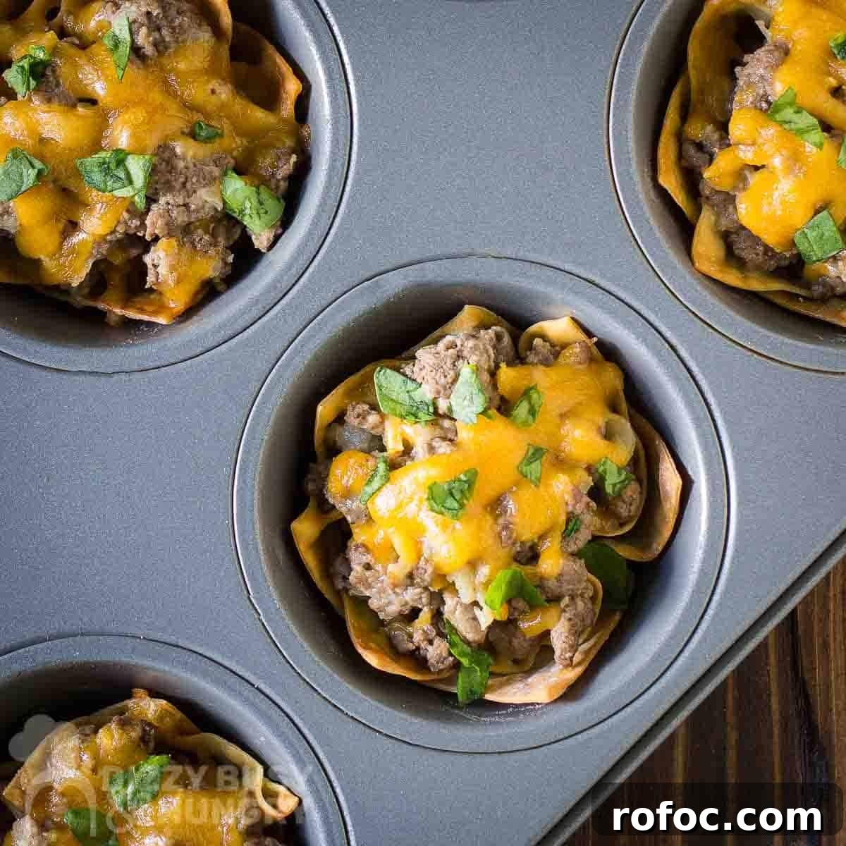 Wonton Cheeseburger Cups: Mini Cheeseburger Bites in Crispy Wrappers 5 Overhead shot of multiple wonton cheeseburger cups in a cupcake sheet on a wooden surface.