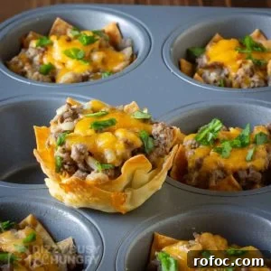 Wonton Cheeseburger Cups: Mini Cheeseburger Bites in Crispy Wrappers 7 Side shot of a wonton cheeseburger cup sitting on a the flat part of a cupcake sheet with more in the background.