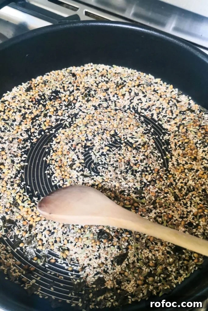 Spiced Dukkah Recipe: Crunchy Egyptian Nut & Spice Mix 4 Seeds being toasted in a large frying pan with a wooden spoon stirring them.