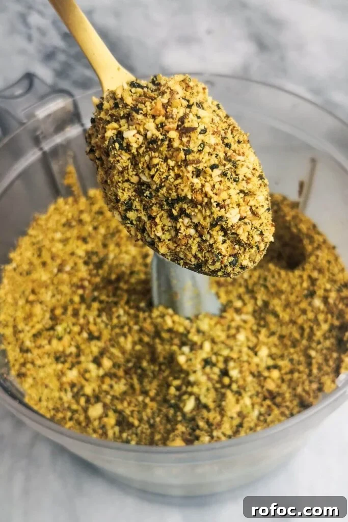 Spiced Dukkah Recipe: Crunchy Egyptian Nut & Spice Mix 7 Close up of blitzed dukkah on a gold spoon with food processor bowl in the background.