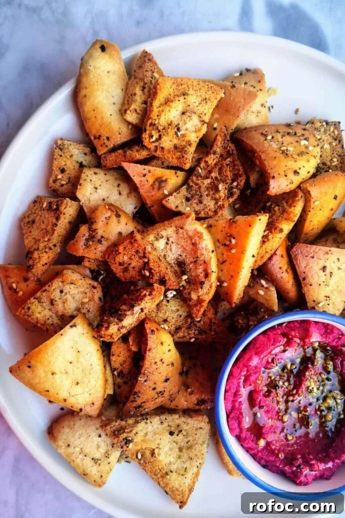 Spiced Dukkah Recipe: Crunchy Egyptian Nut & Spice Mix 8 Pile of homemade pita chips on a white plate with a small bowl of beetroot hummus on the side.