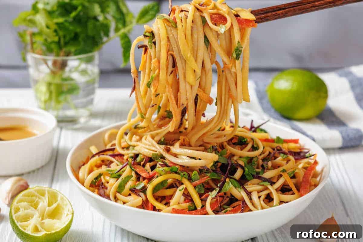 19 Fall Cookout Recipes for Sunday Dinner and Game Day 11 A bowl of Thai Noodle Salad with Mango and Spicy Peanut Dressing is lifted by chopsticks.