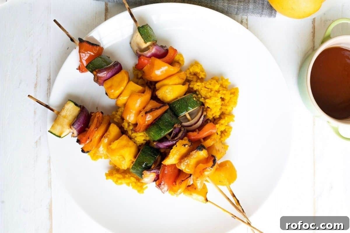 19 Fall Cookout Recipes for Sunday Dinner and Game Day 18 Three Grilled Teriyaki Mango Skewers with bell peppers, zucchini, and onions served on a bed of yellow rice on a white plate.