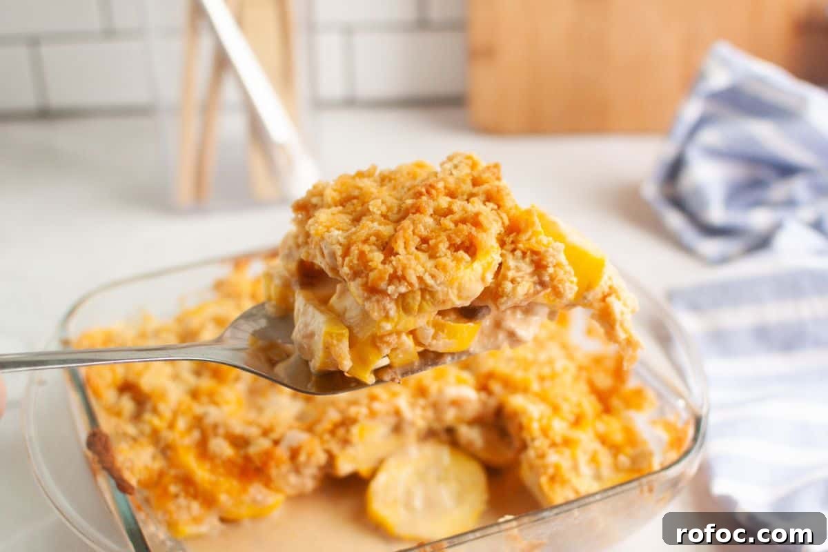 19 Fall Cookout Recipes for Sunday Dinner and Game Day 20 A spoon holds a serving of yellow squash casserole with a crumbly topping above a glass baking dish on a kitchen counter.